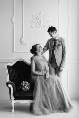 Bej takım elbiseli damat ve lavantalı gelin parlak stüdyoda dar bir gelinlik.