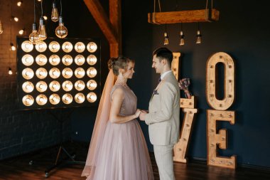 Bej takım elbiseli damat ve lavantalı gelin parlak stüdyoda dar bir gelinlik.