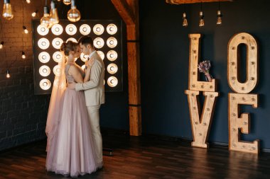 Bej takım elbiseli damat ve lavantalı gelin parlak stüdyoda dar bir gelinlik.