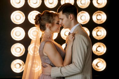 Bej takım elbiseli damat ve lavantalı gelin parlak stüdyoda dar bir gelinlik.