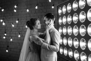 Bej takım elbiseli damat ve lavantalı gelin parlak stüdyoda dar bir gelinlik.