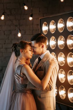 Bej takım elbiseli damat ve lavantalı gelin parlak stüdyoda dar bir gelinlik.