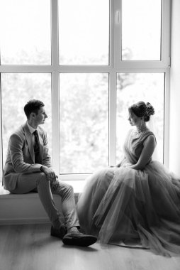 Bej takım elbiseli damat ve lavantalı gelin parlak stüdyoda dar bir gelinlik.