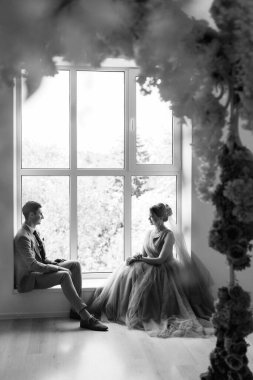 Bej takım elbiseli damat ve lavantalı gelin parlak stüdyoda dar bir gelinlik.