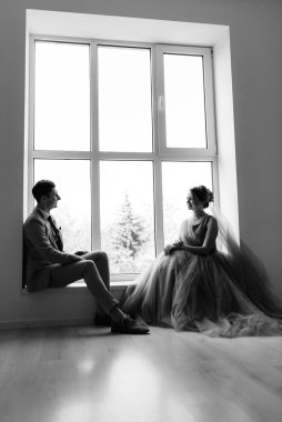 Bej takım elbiseli damat ve lavantalı gelin parlak stüdyoda dar bir gelinlik.