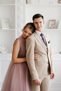 Bej takım elbiseli damat ve lavantalı gelin parlak stüdyoda dar bir gelinlik.