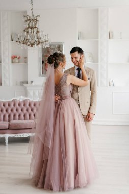 Bej takım elbiseli damat ve lavantalı gelin parlak stüdyoda dar bir gelinlik.