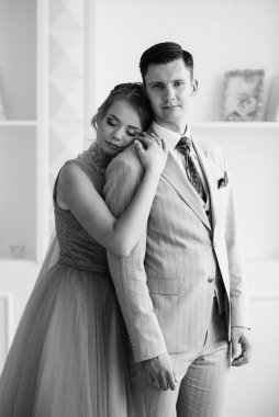 Bej takım elbiseli damat ve lavantalı gelin parlak stüdyoda dar bir gelinlik.