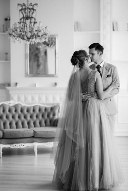 Bej takım elbiseli damat ve lavantalı gelin parlak stüdyoda dar bir gelinlik.