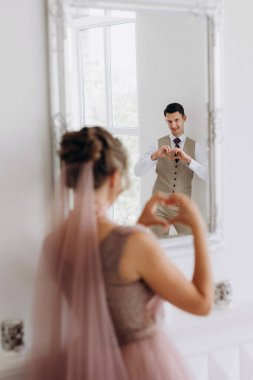 Bej takım elbiseli damat ve lavantalı gelin parlak stüdyoda dar bir gelinlik.