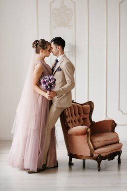 Bej takım elbiseli damat ve lavantalı gelin parlak stüdyoda dar bir gelinlik.