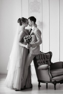 Bej takım elbiseli damat ve lavantalı gelin parlak stüdyoda dar bir gelinlik.