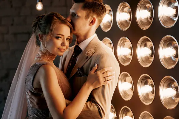 Bej takım elbiseli damat ve lavantalı gelin parlak stüdyoda dar bir gelinlik.