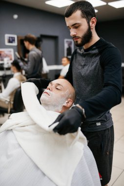 Beyefendinin berber dükkanında sakalını kesen sakallı adam.