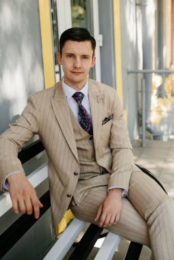 Bankta oturmuş gülümseyen bej takım elbiseli damadın portresi