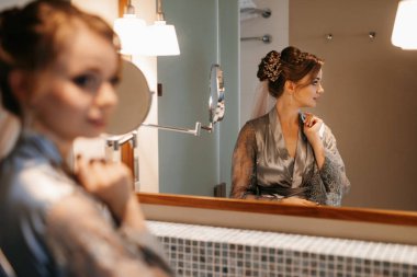 bride in a veil with makeup paints her lips in the bathroom