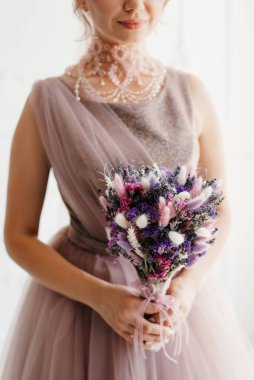 Gelin lavanta renkli pofuduk gelinlik içinde parlak bir stüdyoda buketle