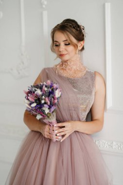 Gelin lavanta renkli pofuduk gelinlik içinde parlak bir stüdyoda buketle