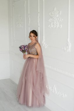 Gelin lavanta renkli pofuduk gelinlik içinde parlak bir stüdyoda buketle