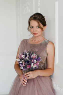 Gelin lavanta renkli pofuduk gelinlik içinde parlak bir stüdyoda buketle