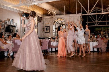 bride in a white dress throws a wedding bouquet to her unmarried girlfriends