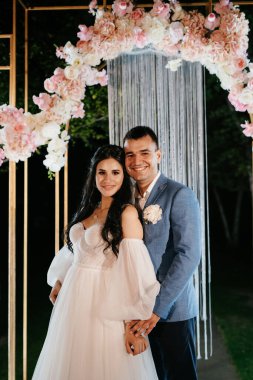 Gelin ve damat, sıcak bir ateş eşliğinde bir akşam düğün kemerine karşı.