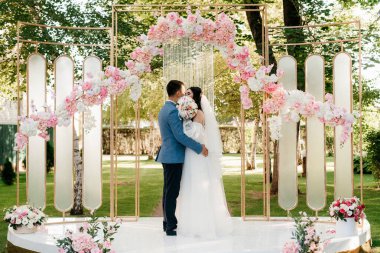 Pembe düğün kemerindeki yeşil parkta bir adamla bir kızın düğün töreni.