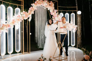 Yeni evliler düğün pastasını mutlu bir şekilde kesiyor, gülüyor ve düğün pastasının tadına bakıyorlar.