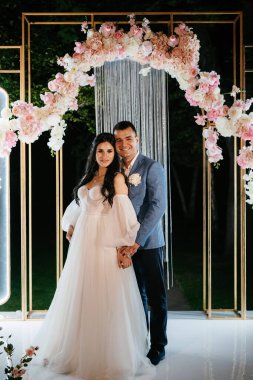 Gelin ve damat, sıcak bir ateş eşliğinde bir akşam düğün kemerine karşı.