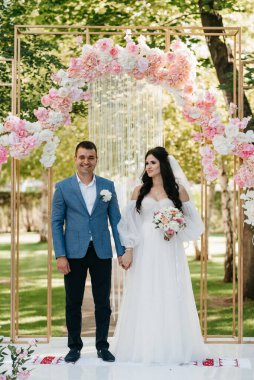 Pembe düğün kemerindeki yeşil parkta bir adamla bir kızın düğün töreni.