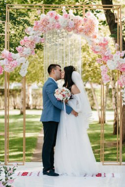 Pembe düğün kemerindeki yeşil parkta bir adamla bir kızın düğün töreni.