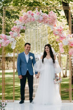 Pembe düğün kemerindeki yeşil parkta bir adamla bir kızın düğün töreni.