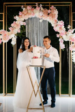 Yeni evliler düğün pastasını mutlu bir şekilde kesiyor, gülüyor ve düğün pastasının tadına bakıyorlar.