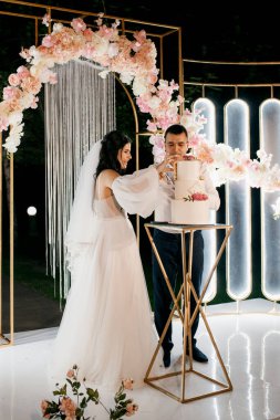 Yeni evliler düğün pastasını mutlu bir şekilde kesiyor, gülüyor ve düğün pastasının tadına bakıyorlar.