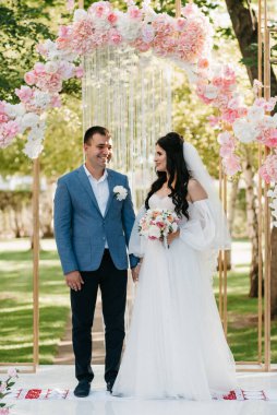 Pembe düğün kemerindeki yeşil parkta bir adamla bir kızın düğün töreni.