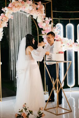 Yeni evliler düğün pastasını mutlu bir şekilde kesiyor, gülüyor ve düğün pastasının tadına bakıyorlar.