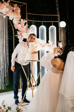 Yeni evliler düğün pastasını mutlu bir şekilde kesiyor, gülüyor ve düğün pastasının tadına bakıyorlar.