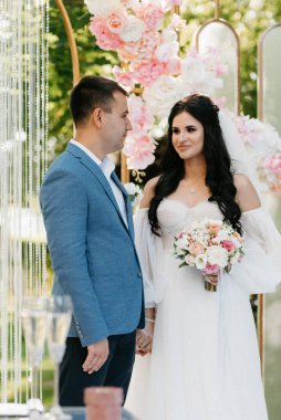 Pembe düğün kemerindeki yeşil parkta bir adamla bir kızın düğün töreni.