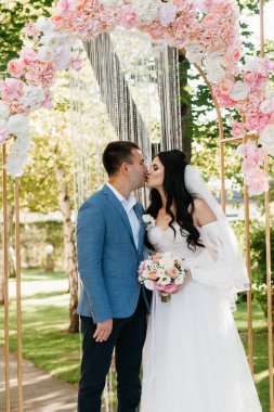 Pembe düğün kemerindeki yeşil parkta bir adamla bir kızın düğün töreni.