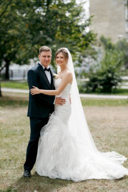 Kahverengi takım elbiseli damat ve şehir ortamında beyaz elbiseli gelin.