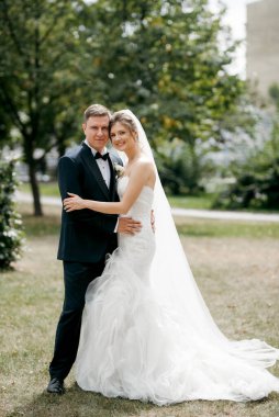 Kahverengi takım elbiseli damat ve şehir ortamında beyaz elbiseli gelin.