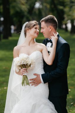 Kahverengi takım elbiseli damat ve şehir ortamında beyaz elbiseli gelin.