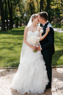 Kahverengi takım elbiseli damat ve şehir ortamında beyaz elbiseli gelin.