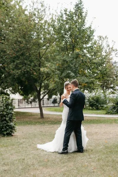 Kahverengi takım elbiseli damat ve şehir ortamında beyaz elbiseli gelin.