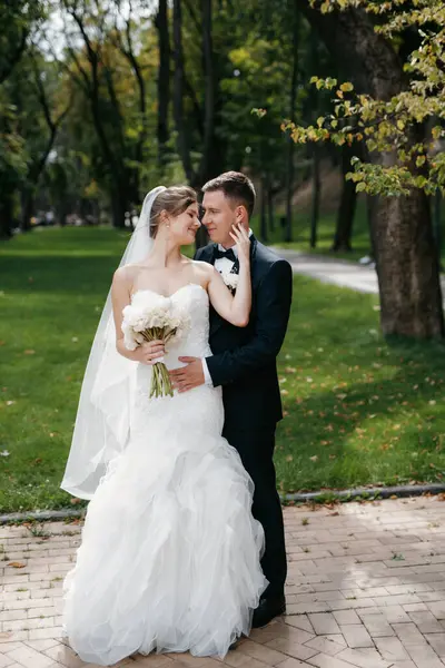 Kahverengi takım elbiseli damat ve şehir ortamında beyaz elbiseli gelin.