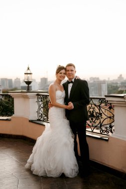 Şehrin ve nehrin zeminine karşı yüksek bir binanın çatısında genç bir çift gelin ve damat