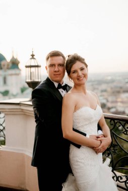 Şehrin ve nehrin zeminine karşı yüksek bir binanın çatısında genç bir çift gelin ve damat