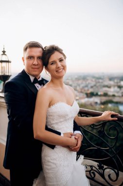 Şehrin ve nehrin zeminine karşı yüksek bir binanın çatısında genç bir çift gelin ve damat