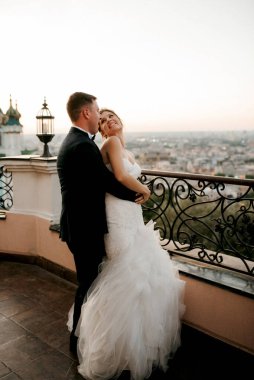 Şehrin ve nehrin zeminine karşı yüksek bir binanın çatısında genç bir çift gelin ve damat