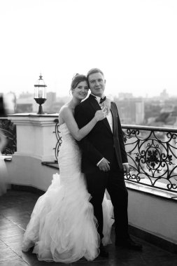 Şehrin ve nehrin zeminine karşı yüksek bir binanın çatısında genç bir çift gelin ve damat